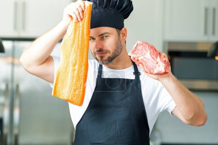 Foto de Hombre cocinero de cocina mantener el pescado y la carne, salmón y carne de res. Chef masculino en uniforme de chefs con carne cruda de res y filete de salmón de pescado. Chef man cocinar carne cruda de res y pescado filete de salmón en la cocina - Imagen libre de derechos