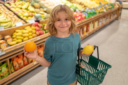 Foto de Niño con limón y naranja. Compras en el supermercado. Niños comprando comestibles en el supermercado. El niño compra verduras frescas en la tienda de comestibles. Niño en la tienda - Imagen libre de derechos