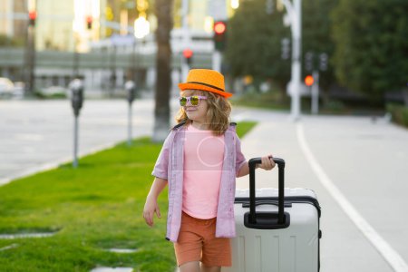 Téléchargez les photos : Portrait d'enfant mode avec bagages, valises en vacances. Mode de vie. Rêves de voyage, d'aventure, de vacances. Petite promenade touristique dans la rue de la ville. Valises et accessoires de voyage - en image libre de droit