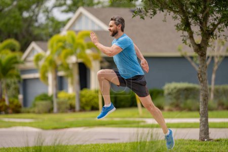 Foto de Un apuesto hombre de mediana edad corriendo por el vecindario americano. Hombre atlético corriendo al aire libre. Estilo de vida saludable. Corredor sano activo trotando al aire libre - Imagen libre de derechos