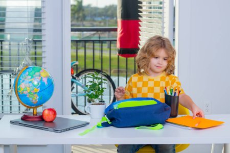 Photo for Nerd school kid doing homework at home. Clever child from elementary school puts school supplies in a backpack. Preparation for school. Smart genius intelligence kid ready to learn. Hard study - Royalty Free Image
