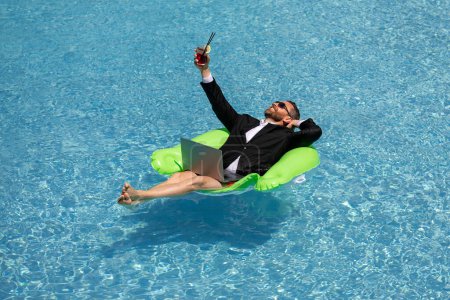 Photo for Freelance work, distance online work, e-working. Summer business. Business man in suit drink summer cocktail and using laptop in pool. Business man dreams on summer business in swimming pool water - Royalty Free Image