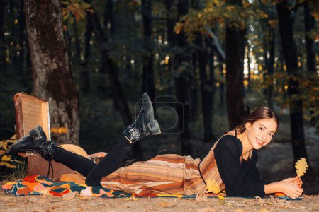 Photo for Young beautiful hipster woman in vintage grunge outfit lie on the autumnal fall orange leaves and hold oak autumn leaf. Girl resting in autumn park. Fall nature beauty concept - Royalty Free Image