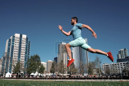 Téléchargez les photos : Toute la longueur de l'homme en bonne santé courir et le sprint à l'extérieur. Modèle masculin en vêtements de sport faisant de l'exercice en plein air dans le parc de la ville. Concept de sport urbain - en image libre de droit