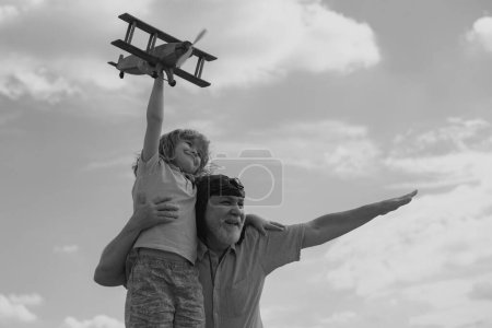 Téléchargez les photos : Incroyable petit-fils enfant et grand-père s'amuser avec avion en plein air sur fond de ciel avec espace de copie. Enfant rêve de voler, enfance heureuse avec grand-père - en image libre de droit