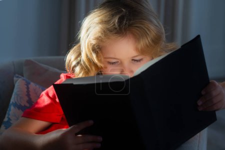 Foto de Primer plano retrato de un niño rubio lindo leyendo una interesante historia de libros para niños. Niño leer libro en casa - Imagen libre de derechos