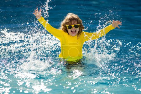 Téléchargez les photos : Enfant excité éclaboussant l'eau dans la piscine. Petit enfant éclaboussant dans l'eau bleue de la piscine. Mignon garçon nageant et éclaboussant d'eau avec des gouttes dans la piscine. éclaboussures d'enfants et de s'amuser au bord de la piscine - en image libre de droit