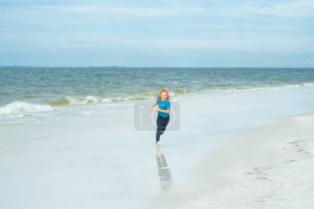 Photo for Cute happy little kid running along the sea coast outdoor on summer beach. Little kid run on summer beach. Excited child run against blue sky and sea. Summer vacation concept. Kids play at the sea - Royalty Free Image