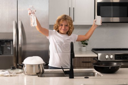 Téléchargez les photos : Nettoyage enfant vaisselle avec éponge. Du matériel de nettoyage. Aide à nettoyer. Tâches ménagères. Il lave la vaisselle. Enfant garçon laver la vaisselle dans l'évier de la cuisine - en image libre de droit