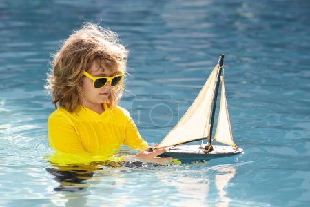 Foto de Un chico jugando en la playa. Niño jugar en el mar con barco de juguete. Niño pequeño que tiene un momento feliz jugar con el barco de juguete en la playa de verano. Vacaciones de verano para niños. Sueño en viaje - Imagen libre de derechos
