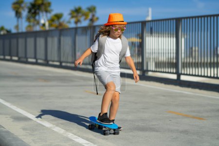 Téléchargez les photos : Un gamin en skateboard. Enfant skateboarder tour sur skateboard dans le parc. Jeune adolescent souriant chevauchant sur un skateboard de croisière moderne, fond urbain - en image libre de droit