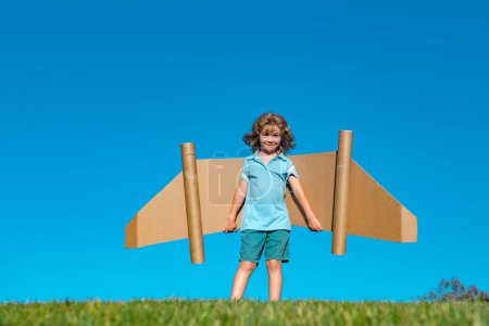 Photo for Happy child playing outside on green grass and blue sky. Kid pilot with toy jetpack. Kid boy play with toy plane cardboard. Summer travel and adventure. Success winner, imagination and dream concept - Royalty Free Image