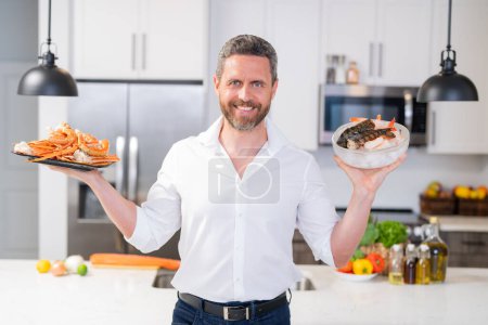 Photo for Man with raw salmon fillet at kitchen. Chef cooking a fish fillet. The big salmon is in the hands of the chef cook. Chef man cooking seafood crab and shrimp, salmon and lobster in home kitchen - Royalty Free Image