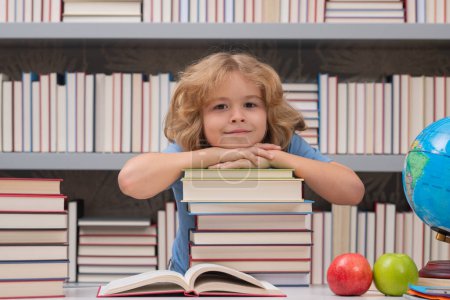 Téléchargez les photos : Un écolier avec une pile de livres à la bibliothèque. Portrait de mignon enfant écolier. L'école et l'éducation concept des enfants. Enfant intelligent avec des fournitures scolaires - en image libre de droit