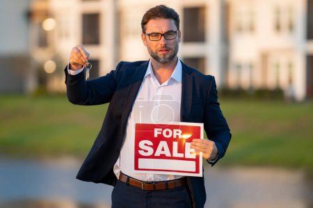 Photo for Successful real estate agent in suit with sign for sale. Real estate broker front of new house. Real estate home owner business man salesman sell house, new apartment in modern building - Royalty Free Image