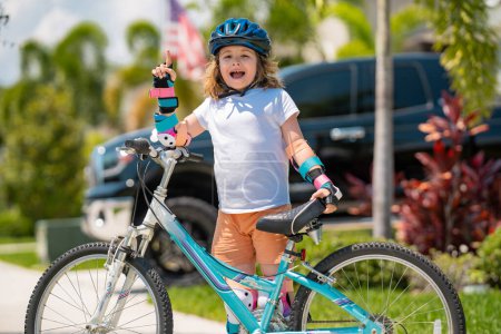 Téléchargez les photos : Un vélo d'enfant. Enfant à vélo. Petit garçon en casque à vélo le long de la piste cyclable. Joyeux petit garçon en vélo. Enfant dans le casque de protection pour vélo à vélo - en image libre de droit