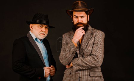 Photo for Head shot portrait of elderly mature dad and grownup son. Two male generations family. Men in hat on dark studio background. Generations family young old - Royalty Free Image