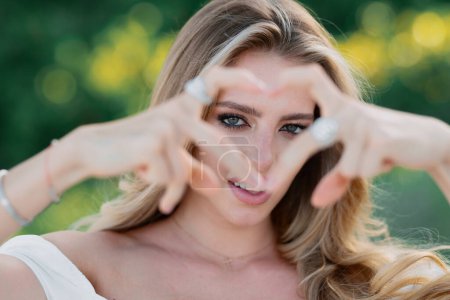 Photo for Sexy woman with sensual look with love heart finger in spring park. Beauty portrait of beautiful female model outside. Woman with beauty face, natural skin on green nature background - Royalty Free Image