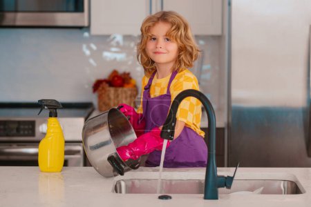 Téléchargez les photos : Un gamin nettoie à la maison. Enfant faisant des travaux ménagers s'amuser. Mignon enfant garçon aider à l'entretien ménager dans la cuisine, nettoyage - en image libre de droit