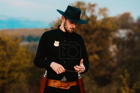 Sheriff or cowboy in black suit. Man with vintage pistol revolver and marshal ammunition. American western Sheriff. Wild west with cowboy