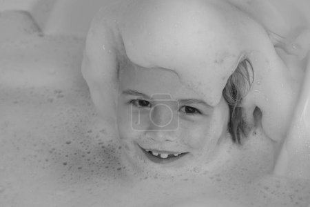Photo for Kids face in foam. Kid having fun in the bath with bubbles. Happy child enjoying bath time. Little boy smiling in the bath with soap foam. Child bathes in a bath with foam - Royalty Free Image