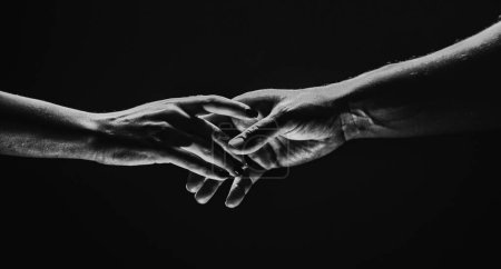 Deux mains s'étirent, fond noir. Couple amoureux tenant des mains, gros plan. Aide main, soutien, amitié