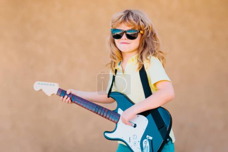 Foto de Gracioso músico hipster niño tocando la guitarra. Gracioso niño rock con guitarra. Un niño con gafas de sol. Concepto de música infantil - Imagen libre de derechos