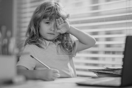 Téléchargez les photos : Fatigué garçon d'école triste tout en faisant des devoirs. L'enfant tient un crayon et dessine à la maison. écolier adolescent dessin assis à la table - en image libre de droit