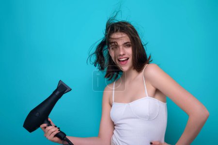 Photo for Young woman drying her hair with a hairdryer isolated on studio background. Young woman with blow dryer drying hair, making hairdo. Close up portrait of beautiful young woman in drying hairstyle - Royalty Free Image