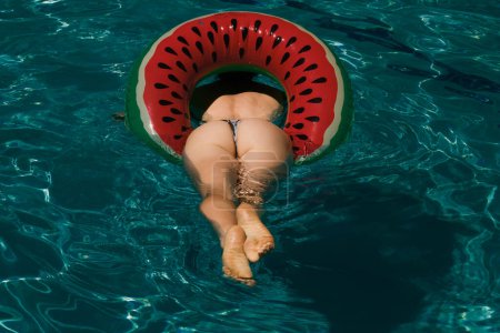 Foto de Summer Vacation. Enjoying suntan. Woman in bikini on the inflatable mattress in the swimming pool. Close-up rear back of nice girl posing with round shape booty in bikini, close up butt - Imagen libre de derechos