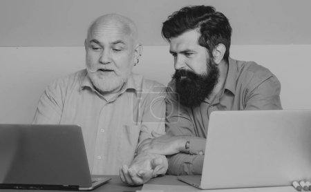 Téléchargez les photos : Deux hommes d'affaires assis à la table tapant sur ordinateur portable travaillant avec un nouveau plan d'affaires. Deux hommes d'affaires. Employés de bureau - en image libre de droit