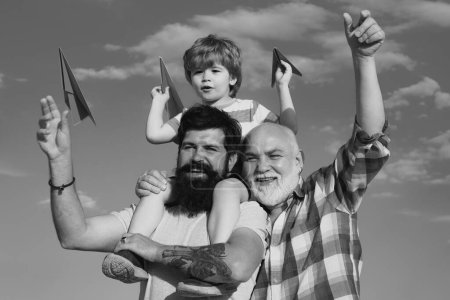 Foto de Generación de hombres: el abuelo, el padre y el nieto se abrazan mirando a la cámara y sonriendo. Tres generaciones diferentes: abuelo e hijo juntos. Concepto de infancia - Imagen libre de derechos