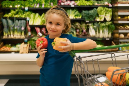 Foto de Niño con verduras y pimientos en la tienda de comestibles. Niño eligiendo frutas y verduras durante las compras en el supermercado de verduras. Un niño yendo de compras. Comida saludable para niños - Imagen libre de derechos