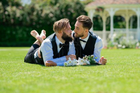 Photo for Gay couple laying on grass on wedding day. Married LGBT couples celebrate a romantic wedding ceremony together with a bouquet flower. Portrait of gay couple in love on wedding day. Gay wedding outdoor - Royalty Free Image