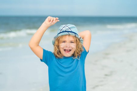 Photo for Summer vacation concept. Happy little kid walking on sea sandy beach. Travel and adventure kids concept. Lovely kid play outdoor. Pretty little child in hat relaxing on the beach near sea, summer - Royalty Free Image