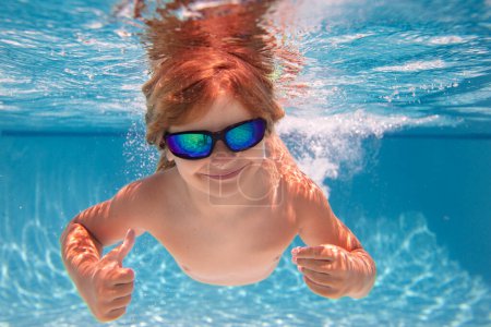 Téléchargez les photos : Enfant nageant sous l'eau avec les pouces levés. Un enfant sous-marin nage dans la piscine. Enfant garçon nageant et plongeant sous l'eau dans la piscine. Vacances d'été en famille avec enfants. Piscine sous-marine enfants - en image libre de droit