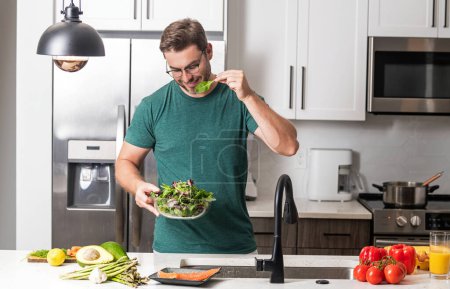 Photo for Man with a plate of vegetable salad in the kitchen. Man cooking vegan healthy salad in kitchen. Millennial man at modern kitchen with vegetables, prepare fresh vegetable salad for dinner or lunch - Royalty Free Image