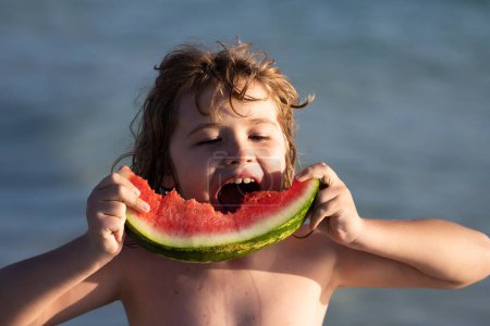 Téléchargez les photos : Joyeux enfant sur la mer avec pastèque. Un enfant drôle mange de la pastèque. Enfant relaxant sur la plage de la mer d'été. Enfant avec des fruits d'été dans la piscine. Vacances d'été avec les enfants. Enfant avec un morceau de pastèque - en image libre de droit