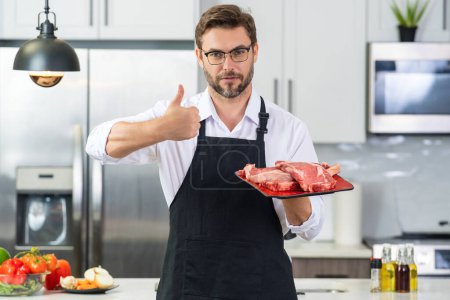 Photo for Health, natural protein concept. Handsome man in kitchen cooking meat beef in the kitchen. Healthy food concept. Healthy diet, meat protein. Fork veal filet, roasting beef steak. Raw beef steak - Royalty Free Image
