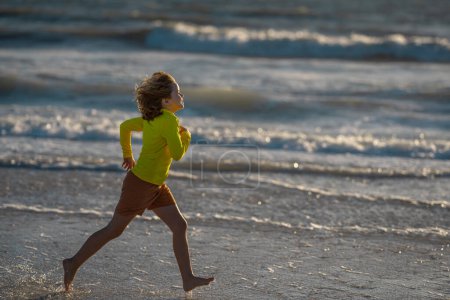 Photo for Exited carefree little boy running on wet coast near waving sea on sunny summer day. Kid running at summer beach. Carefree child. Excited child running in the summer sea. Cute kid run on summer sea - Royalty Free Image
