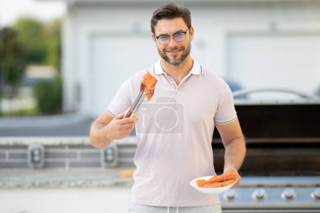 Photo for Handsome man preparing barbecue. Male cook cooking salmon fish on barbecue grill. Guy cooking salmon fish on barbecue for summer family dinner at the backyard of the house - Royalty Free Image