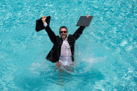 Téléchargez les photos : Homme d'affaires en costume et ordinateur portable éclaboussent l'eau dans la piscine. Fou vacances d'affaires d'été. Drôle excité homme d'affaires étonné dans l'usure formelle saut dans l'eau au bord de la piscine. Chaud été affaires - en image libre de droit