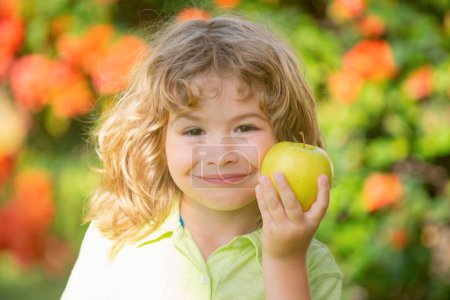 Photo for Portrait of little boy holding and eating an apple over green nature background - Royalty Free Image