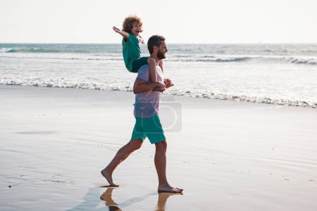 Foto de Padre e hijo caminando sobre el mar. Hombre guapo padre llevando un hijo joven. Feliz padre sosteniendo al niño. Papá con niño en un día de verano. Concepto de familia amigable y de vacaciones de verano - Imagen libre de derechos