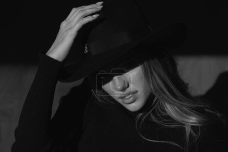 Photo for Girl in fashion hat. Sexy gorgeous woman with shadows on beautiful face on black studio. Hidden eyes with wide broad brim hat - Royalty Free Image