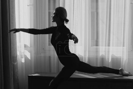 Photo for Ballet dancer. Home workout. Young female woman workout, fitness training at home near window. Girl stretching fit body - Royalty Free Image