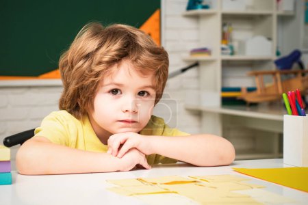 Foto de Niño lindo en el aula cerca del escritorio de pizarra. Niños de primaria - Imagen libre de derechos