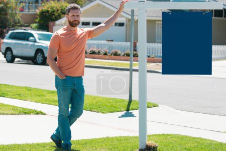 Téléchargez les photos : Agent immobilier professionnel avec maison à vendre signe debout près de la propriété résidentielle à l'extérieur. Espace de copie - en image libre de droit