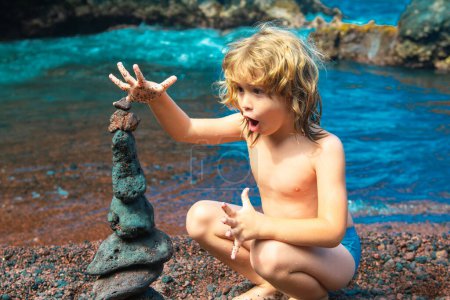 Téléchargez les photos : Enfant excité faisant pyramide de pierres sur la plage de galets symbolisant la stabilité, zen, harmonie, équilibre - en image libre de droit
