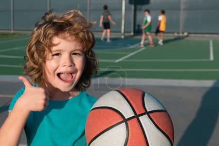 Foto de Lindo chico sonriente juega baloncesto mostrar pulgares hacia arriba signo. Lindo niño sonriente juega baloncesto - Imagen libre de derechos